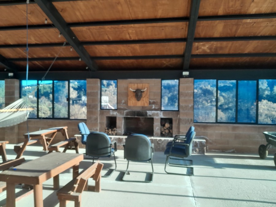 La chimenea dentro de la nave, con sillas y mesas de madera alrededor y el campo detrás de los ventanales.