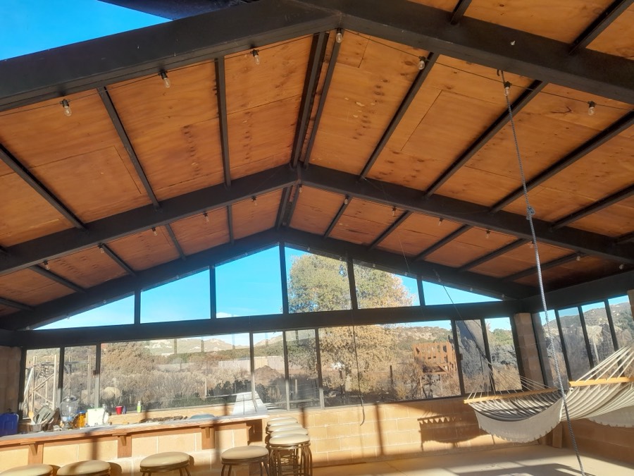 El interior de la nave: techo de madera a dos aguas, el hastial de vidrio y una hamaca colgada junto a los ventanales.